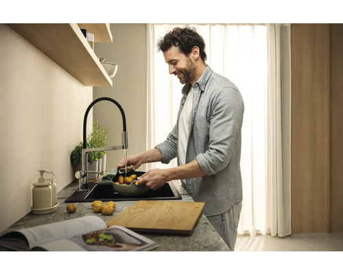 Un homme lave des pommes de terre dans un évier avec un robinet de cuisine dans une cuisine moderne.