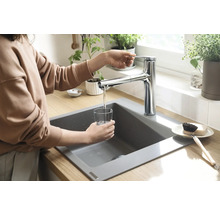 Frau füllt ein Glas Wasser an einem Spültisch mit einer Armatur.