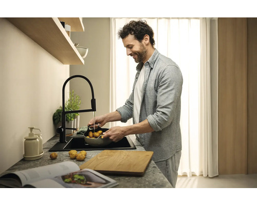 Homme lavant des pommes de terre dans une cuisine moderne avec évier et robinet noirs.