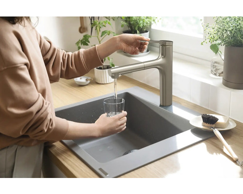 Eine Person füllt ein Glas Wasser an einem Spültisch mit Armatur in einer Küche.