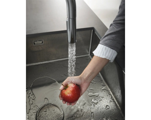 Eine Person wäscht einen Apfel unter einem Wasserhahn in einer Spüle.