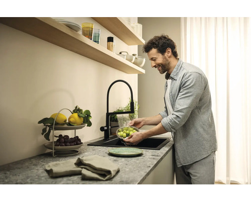 Un homme lave des fruits dans un évier de cuisine avec un robinet noir