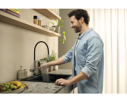 Un homme utilise un robinet de cuisine avec douchette sur un évier moderne