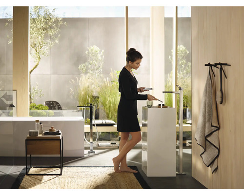 Salle de bains lumineuse avec baignoire îlot, colonne de lavabo et femme