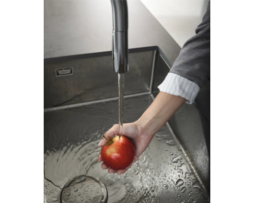 Ein Apfel wird in einer Edelstahlspüle unter einem Wasserhahn gewaschen.