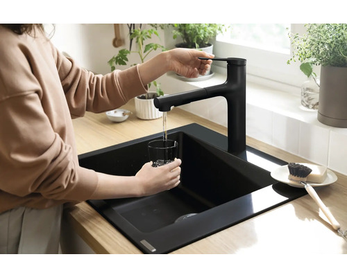 Frau füllt ein Glas Wasser an einem schwarzen Küchenspülbecken mit Wasserhahn