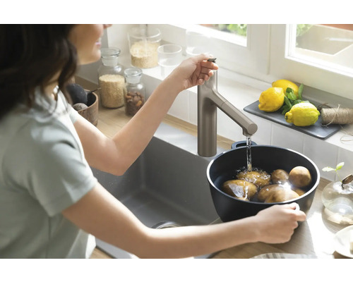 Frau wäscht Kartoffeln in einer Spüle mit Wasserhahn.