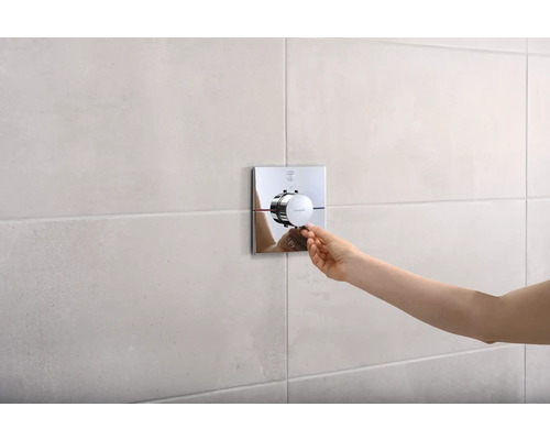 Main actionnant la robinetterie de douche Hansgrohe sur un mur carrelé