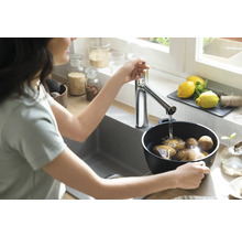 Frau befüllt Topf mit Kartoffeln am Küchenspültisch unter Wasserhahn