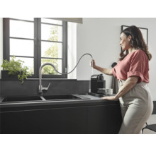 Moderne Küche mit Doppelspüle, Armatur und Kaffeemaschine, eine Frau befüllt die Kaffeemaschine mit Wasser.