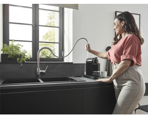 Moderne Küche mit Doppelspüle, Armatur und Kaffeemaschine, eine Frau befüllt die Kaffeemaschine mit Wasser.