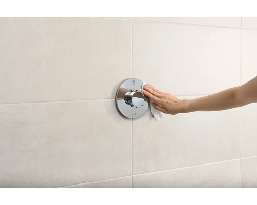 Hand reinigt eine verchromte Duscharmatur mit einem Tuch