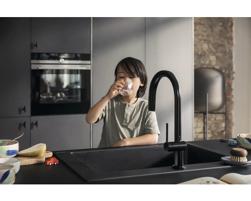 Kind trinkt Wasser in einer modernen Küche mit schwarzem Spülbecken und Armatur