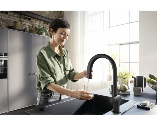 Frau befüllt Glas unter schwarzer Küchenarmatur