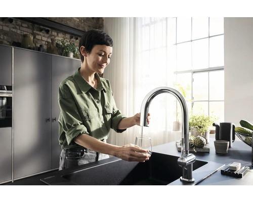 Frau füllt Wasser in ein Glas am Spültisch mit einer Armatur in einer Küche.