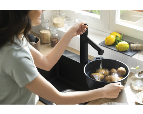 Eine Person befüllt einen Topf mit Kartoffeln unter einem Wasserhahn in einer Küche.