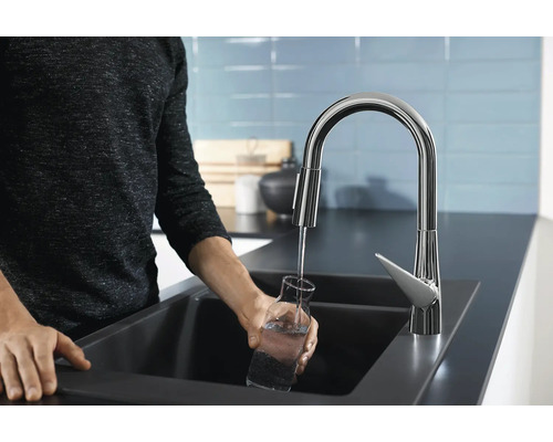 Une personne remplit un verre d''eau à un évier avec un robinet.