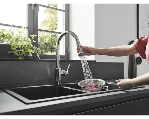 Une personne lave des fruits rouges dans une passoire sous un robinet de cuisine dans une cuisine moderne.