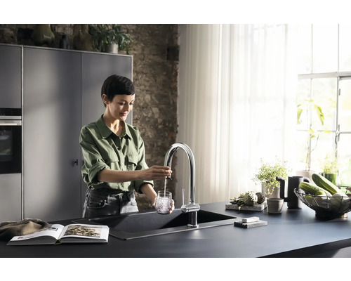 Frau füllt Wasser in einem modernen Küchenspülbecken in ein Glas