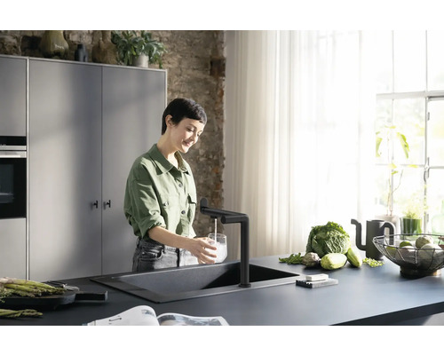 Une femme remplit un verre d''eau à un évier de cuisine avec un robinet dans une cuisine lumineuse.
