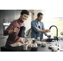 Szene in einer Küche mit zwei Personen, die Kaffee zubereiten, mit einem Wasserkocher, einer Kaffeemaschine und einer Küchenarmatur.