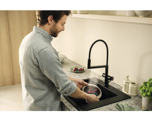 Un homme lave des baies dans un évier de cuisine noir avec un robinet.