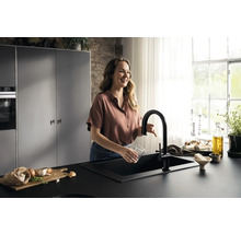 Femme rinçant un verre dans un évier de cuisine noir avec robinet