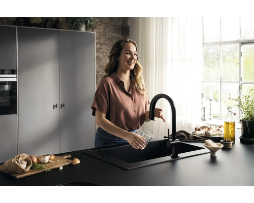 Frau spült Glas am schwarzen Küchenwaschbecken mit Armatur in Küche