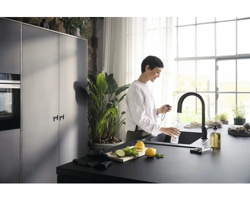 Eine Frau befüllt eine Flasche mit Wasser aus einem schwarzen Wasserhahn in einer modernen Küche.