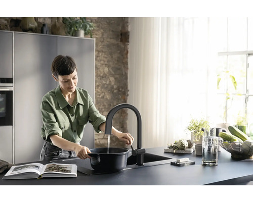 Frau füllt Wasser in einen Topf an einem Küchenspültisch mit Armatur
