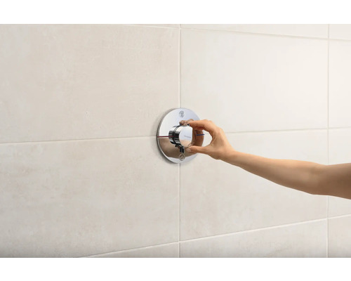 Hand bedient einen runden, metallenen Duschmischer an einer gefliesten Wand