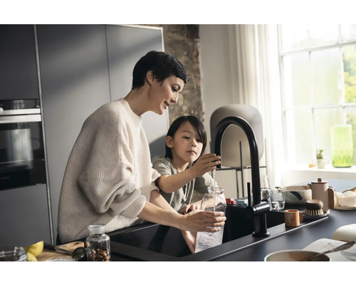 Mutter und Kind füllen eine Glasflasche mit einem Wasserhahn in einer modernen Küche.