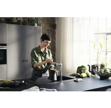 Femme remplissant une cruche d''eau à un robinet de cuisine dans une cuisine moderne.