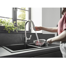 Frau wäscht Himbeeren in einem Sieb unter einem Wasserhahn in einer modernen Küche mit Doppelspüle