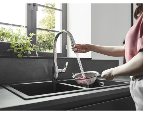 Frau wäscht Himbeeren in einem Sieb unter einem Wasserhahn in einer modernen Küche mit Doppelspüle