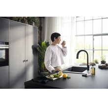 Moderne Küche mit schwarzer Spüle, Armatur und einer Frau, die ein Glas Wasser trinkt
