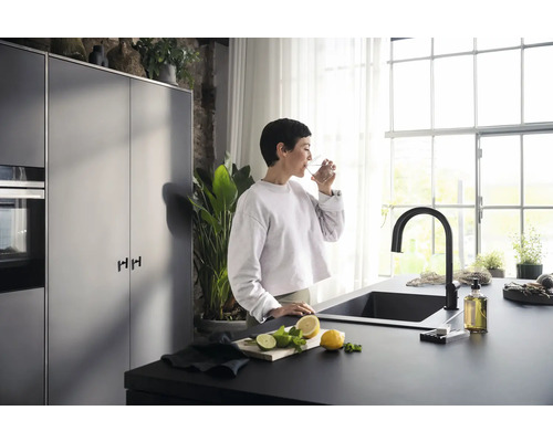 Moderne Küche mit schwarzer Spüle, Armatur und einer Frau, die ein Glas Wasser trinkt