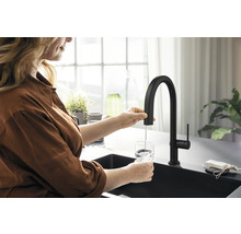 Une femme remplit un verre d''eau sous un robinet noir dans une cuisine