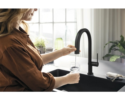 Frau füllt Wasser in ein Glas unter einem schwarzen Küchenarmatur