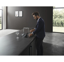Mann spült Glas in moderner Küche mit Spültischarmatur.