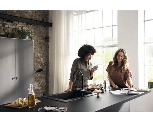 Helle Küche mit zwei Frauen an einer schwarzen Arbeitsplatte mit Spüle und Armatur.