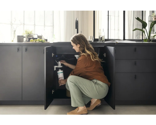 Frau wechselt Wasserfilter unter der Spüle in einer modernen Küche.