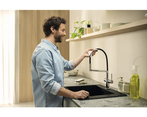 Un homme nettoie un robinet de cuisine avec un évier noir et un plan de travail