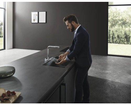 Un homme fait la vaisselle dans une cuisine moderne avec évier et robinet.