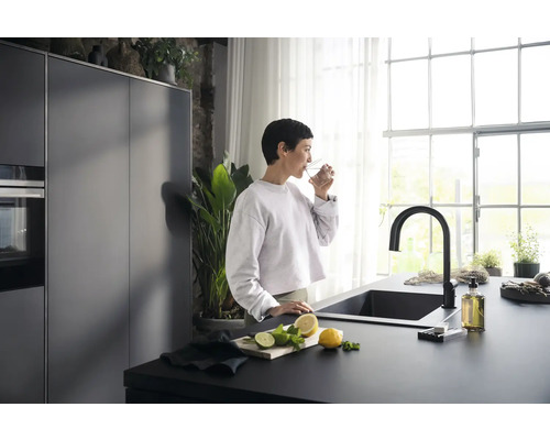 Moderne Küche mit dunkler Spüle, Armatur und einer Frau, die ein Glas Wasser trinkt