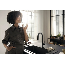 Cuisine lumineuse avec évier noir, robinet et femme tenant un verre d''eau