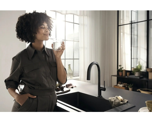 Helle Küche mit schwarzem Spülbecken, Wasserhahn und Frau, die ein Glas Wasser hält