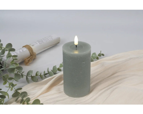 Bougie pilier LED décorative avec plantes et un rouleau sur un tissu beige
