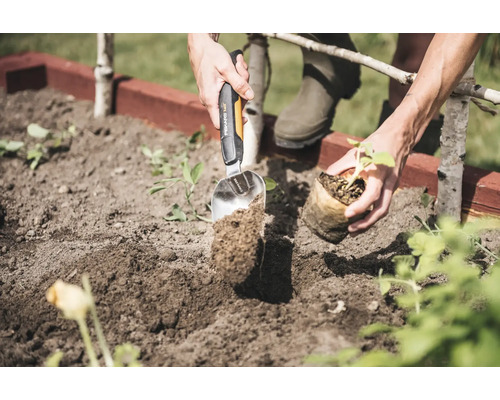 Une personne plante une plante dans un jardin à l''aide d''une plantoir.