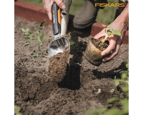 Scène de jardinage avec une personne plantant un végétal à l''aide d''une truelle en acier inoxydable de marque Fiskars